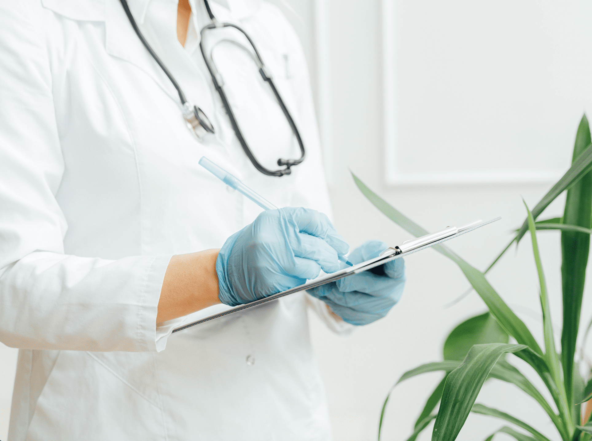 A doctor, wearing blue hygiene gloves, is writing in a patient file.