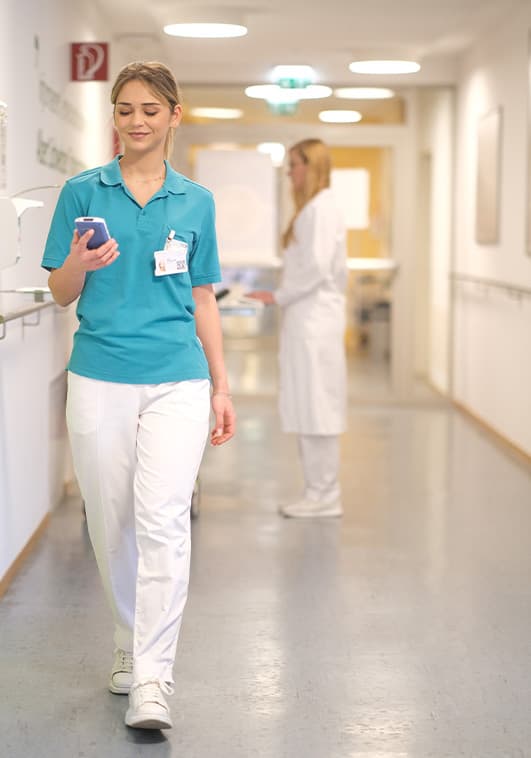 A young doctor is walking through a hospital. She is looking at the ilviCLINIC device in her hand. STEADYTEMP® can be used on this device.